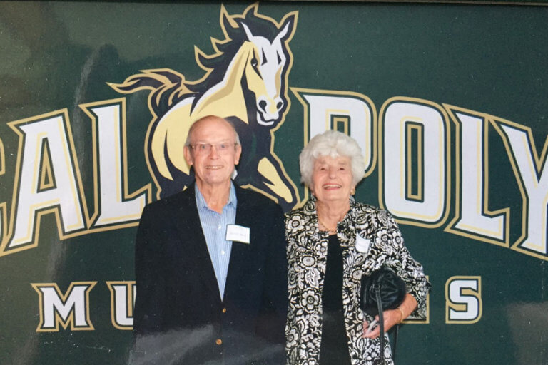 George and Tonny Murray smiling in front of Cal Poly Mustangs banner