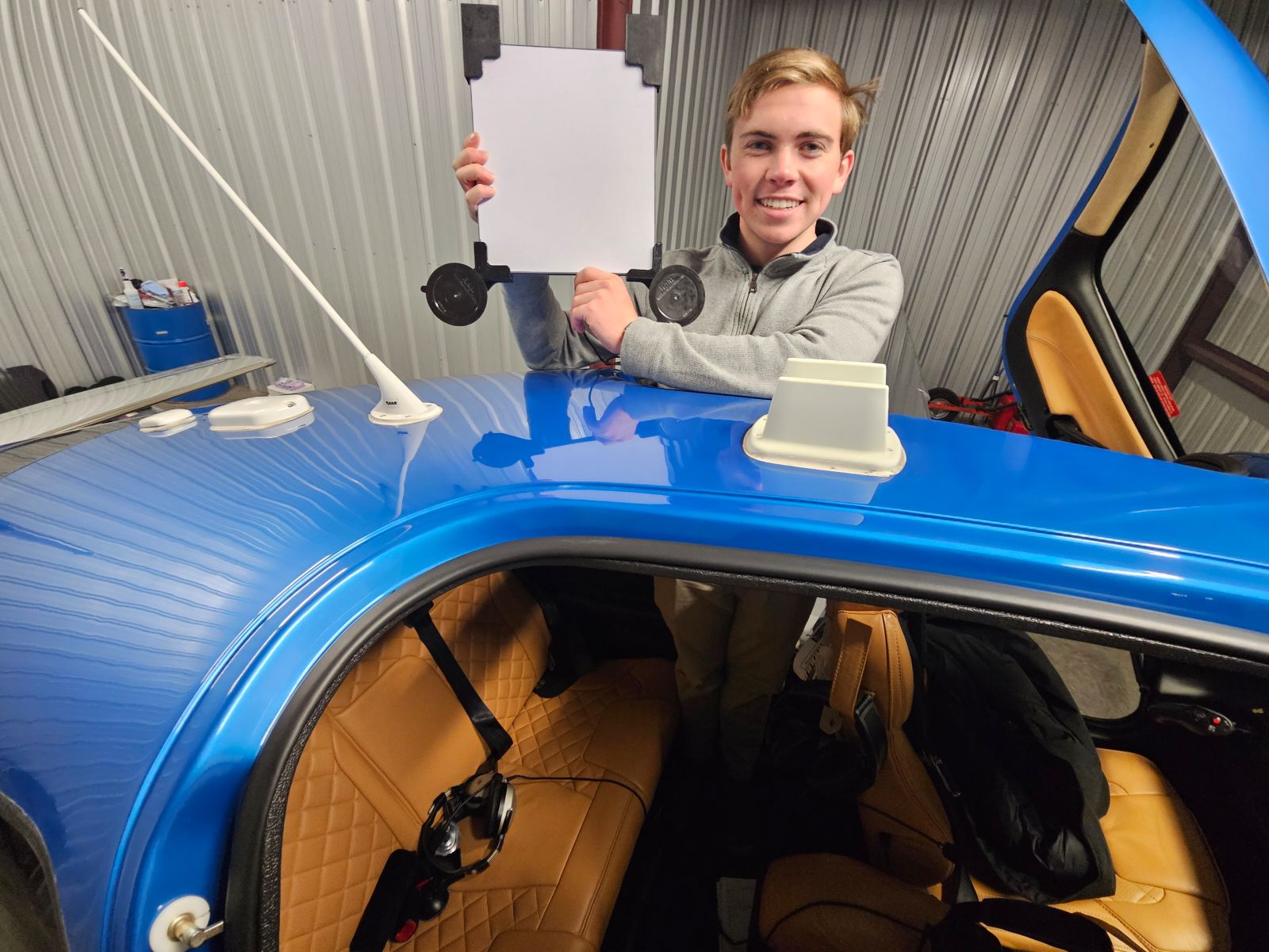 Cal poly student Andrew Chapin holding up one of his inventions - a white mount with suction cups used as a screen or monitor for passengers to use while flying in private planes.